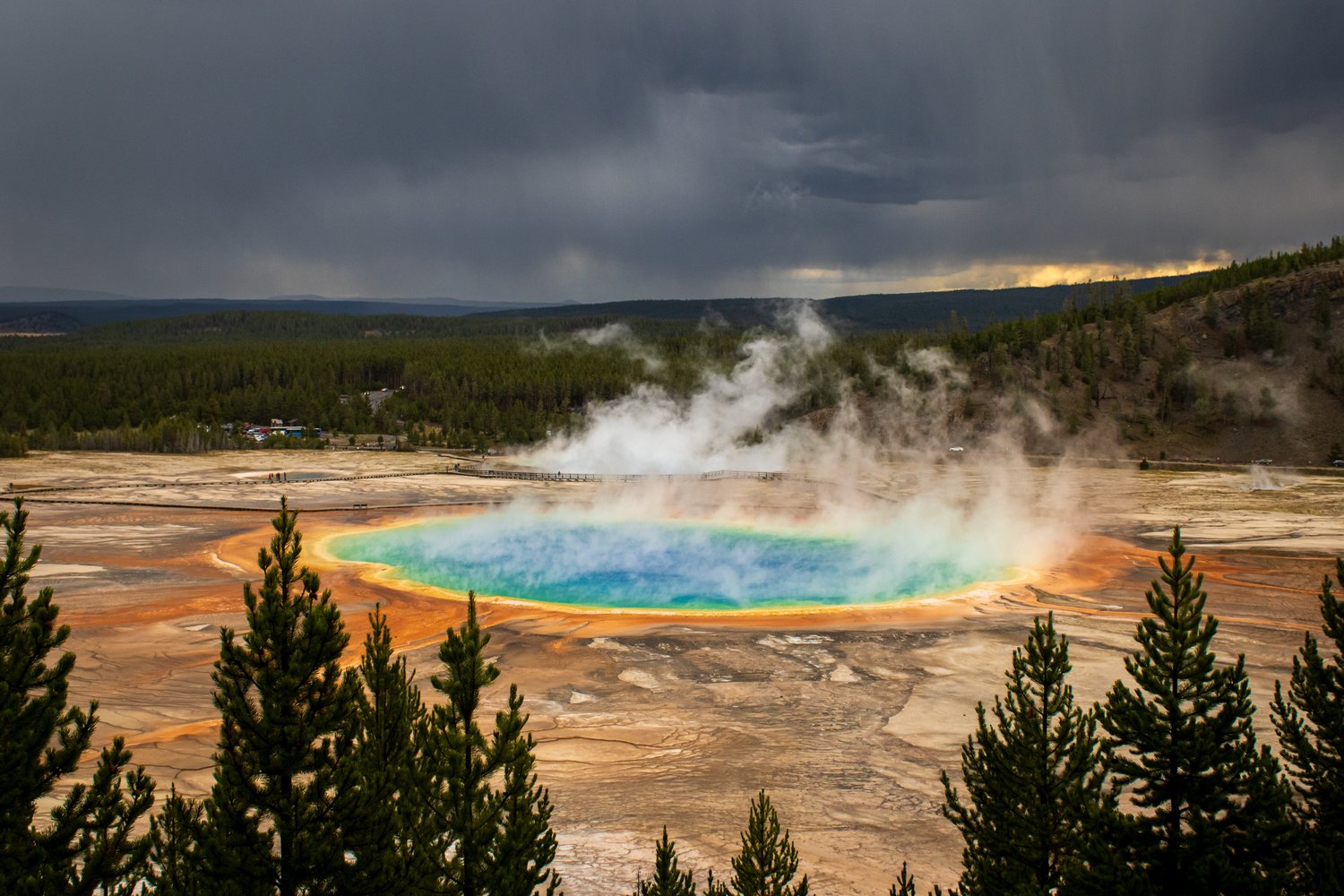 Grand Prismatic Spring from the overlook, its blue centre ringed in orange and green under a storm sky.